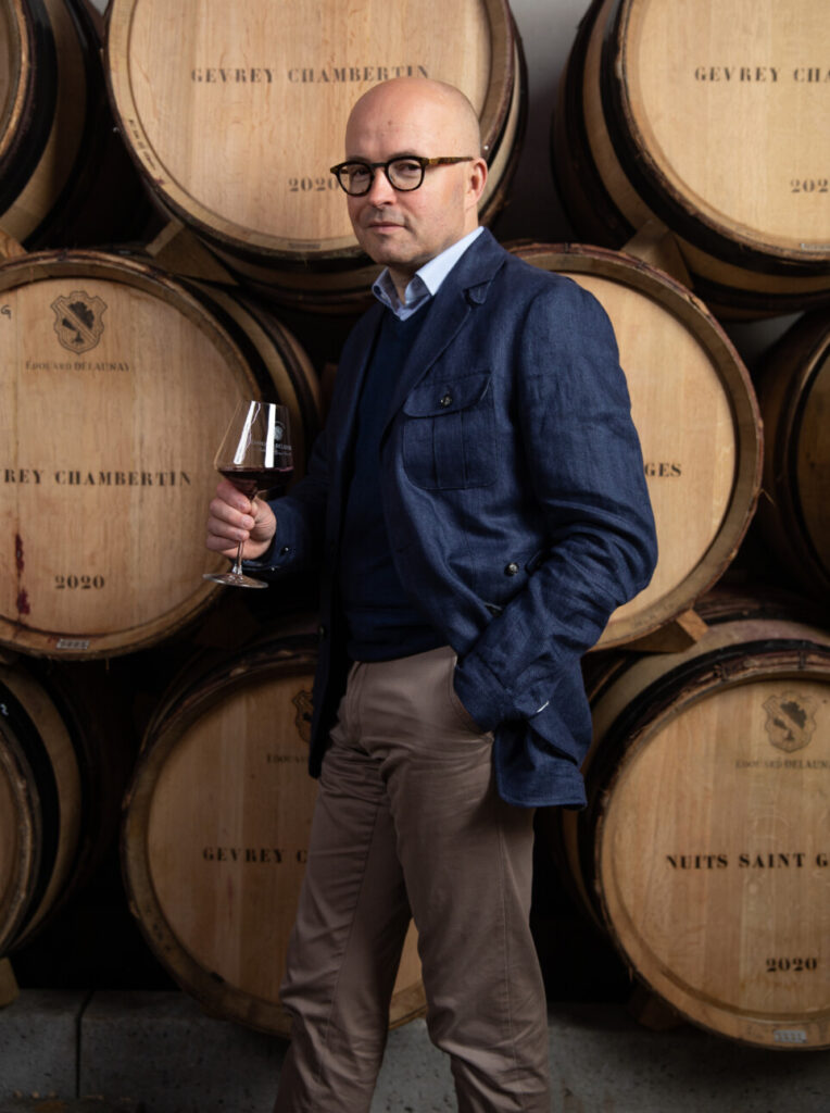 Laurent Delaunay, un verre à la main devant les barriques de la maison