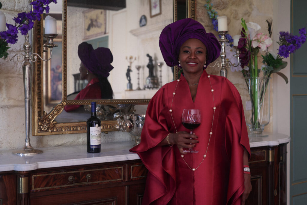 Lili Renée en robe rouge, un verre de vin à la main