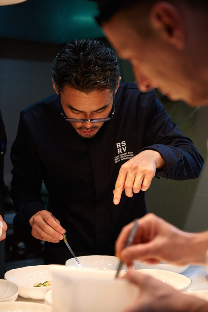 Le chef japonais Hideaki Sato qui cuisine au dessus d'une assiette blanche 